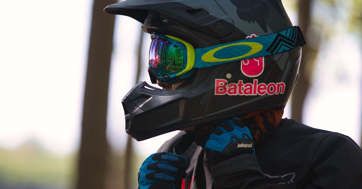 Motocross rider in gear adjusting helmet for safety outdoors. Focus on protective equipment.