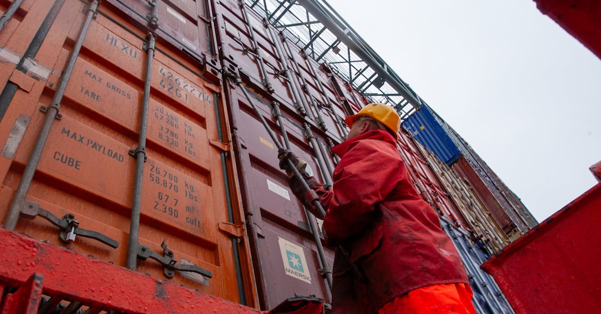 Industrial worker securing cargo containers on a rainy day at a shipping port.