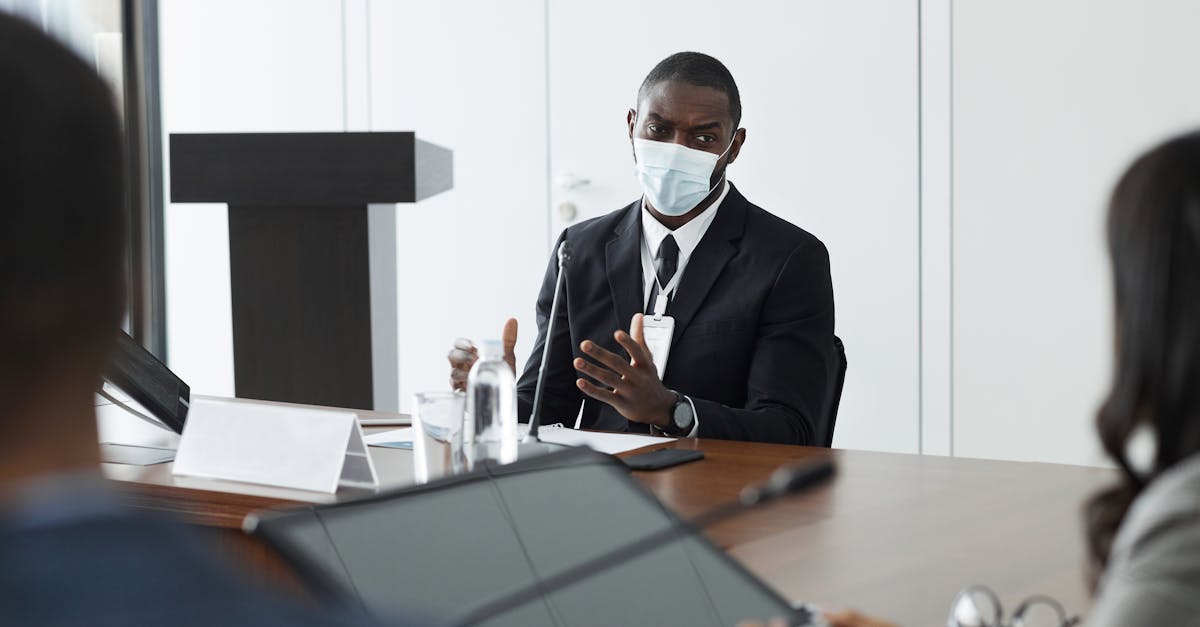 A masked professional speaks at a formal meeting, emphasizing safety and communication.