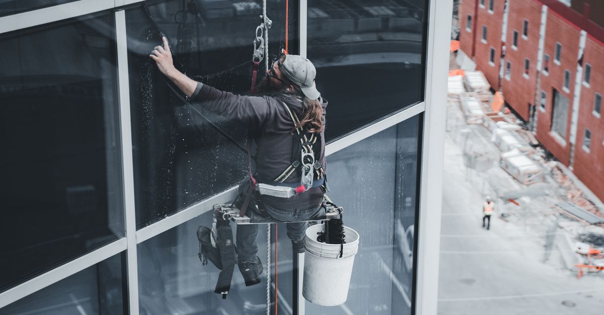 A worker cleaning skyscraper windows with a harness in an urban setting.