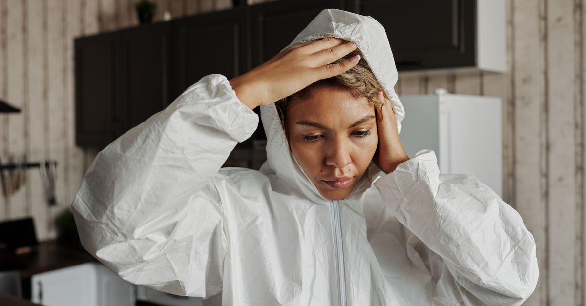A woman wearing white protective gear appears contemplative inside a modern kitchen.