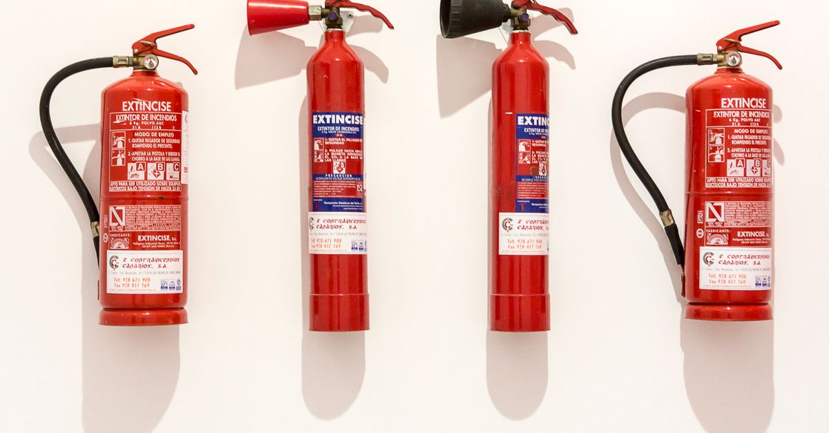 Four red fire extinguishers hanging on a clean white wall in an orderly fashion.