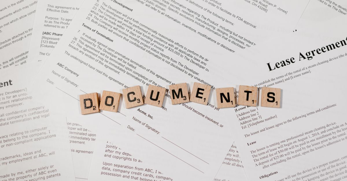 Top view of scrabble tiles spelling 'DOCUMENTS' on various contracts and agreements.