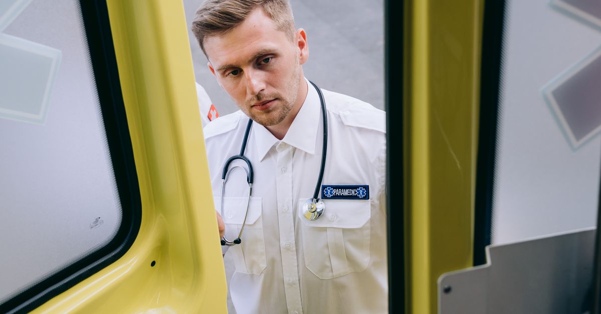 Caucasian male paramedic standing outside an ambulance vehicle, focused and ready for duty.
