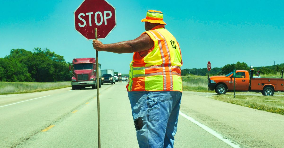 Road construction worker holding a stop sign on a highway ensuring traffic safety.