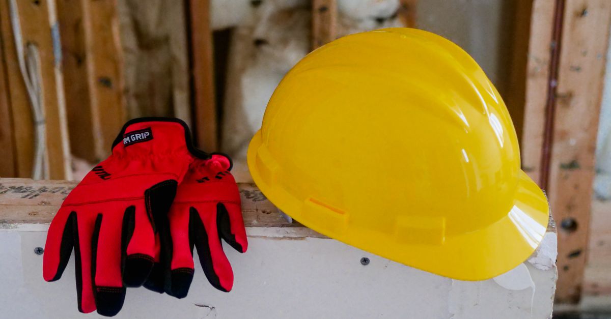 Close-up of a yellow hard hat and red gloves on a construction site, symbolizing safety and work.
