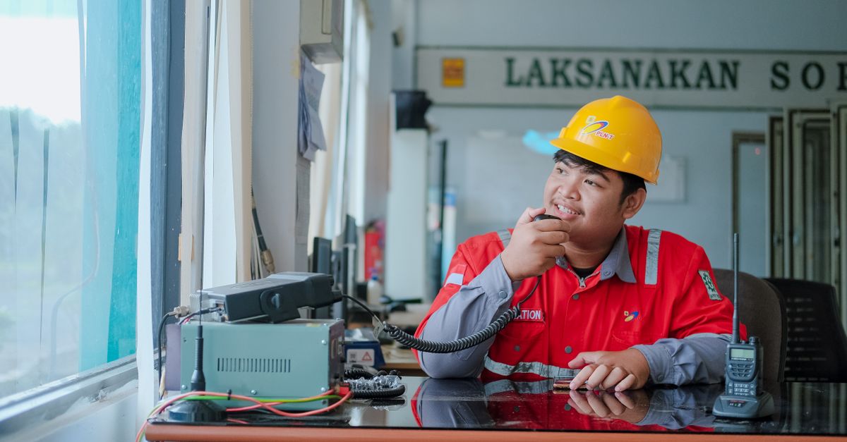 Smiling construction worker in hard hat using a two-way radio indoors for communication.