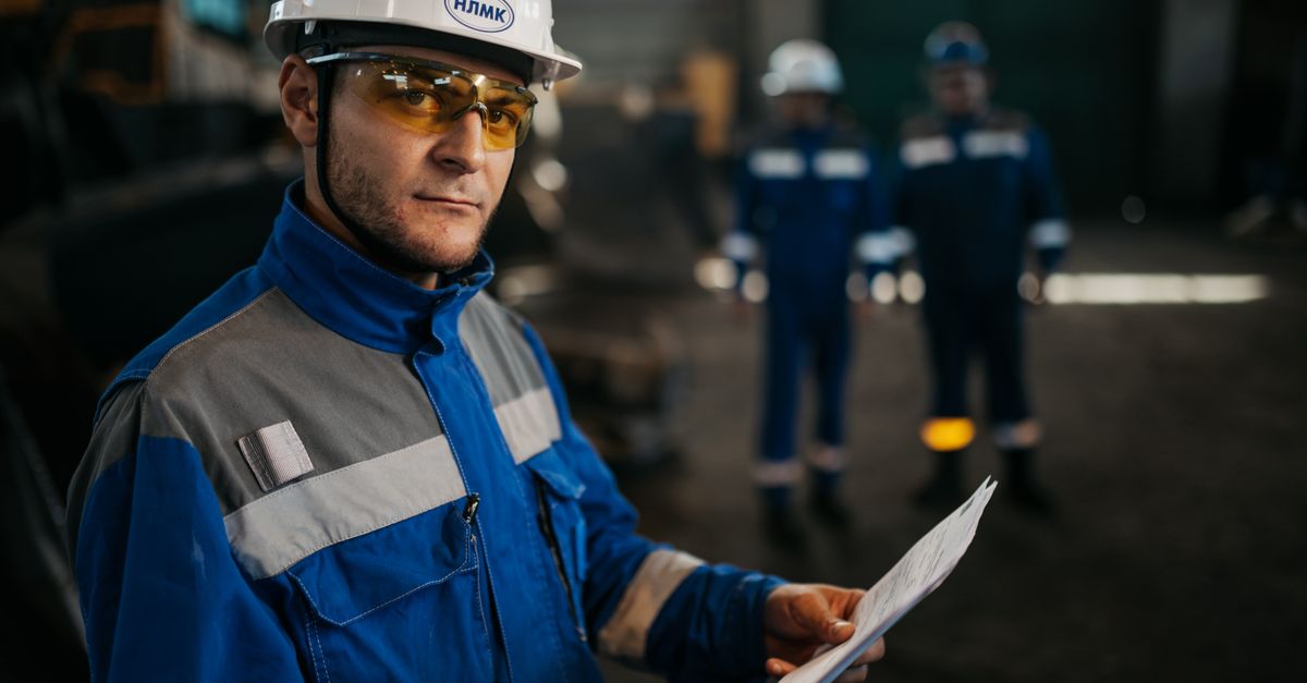 Focused industrial worker in protective gear reviewing documents in a factory setting in Russia.