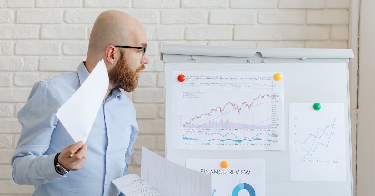 Bald businessman in smart casual attire analyzing financial charts on a whiteboard in an office setting.