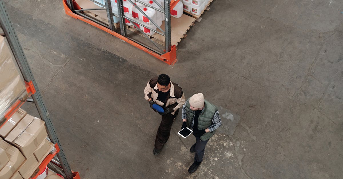 Two workers discussing inventory in a warehouse, using a digital tablet for coordination.