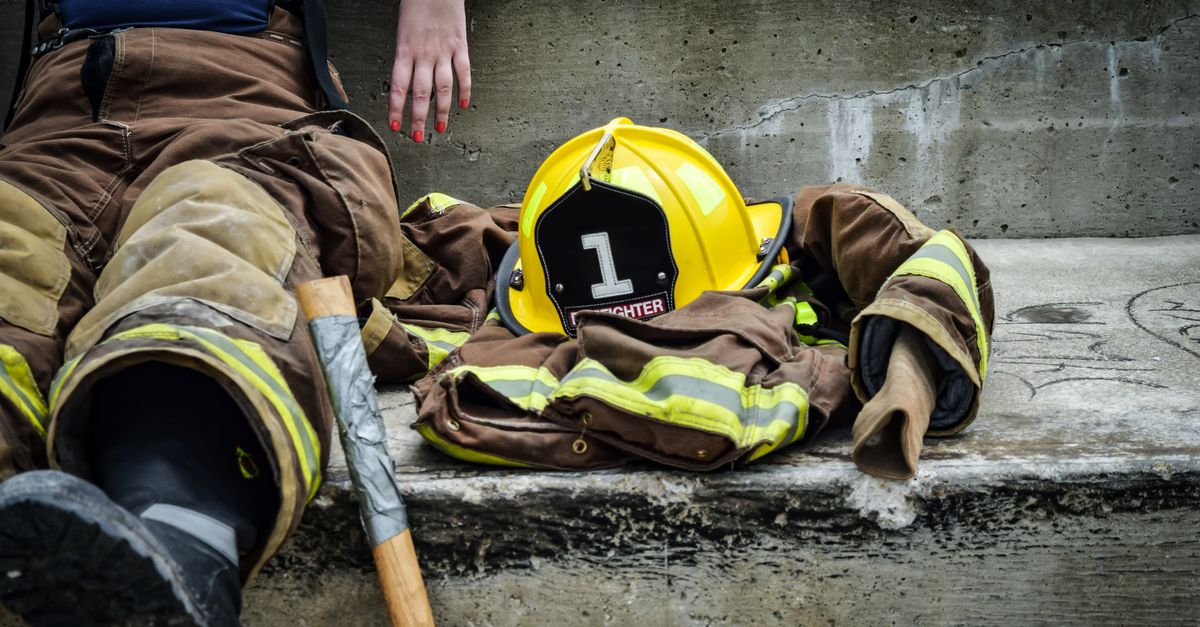 Firewoman taking a break on concrete steps with gear and helmet nearby.