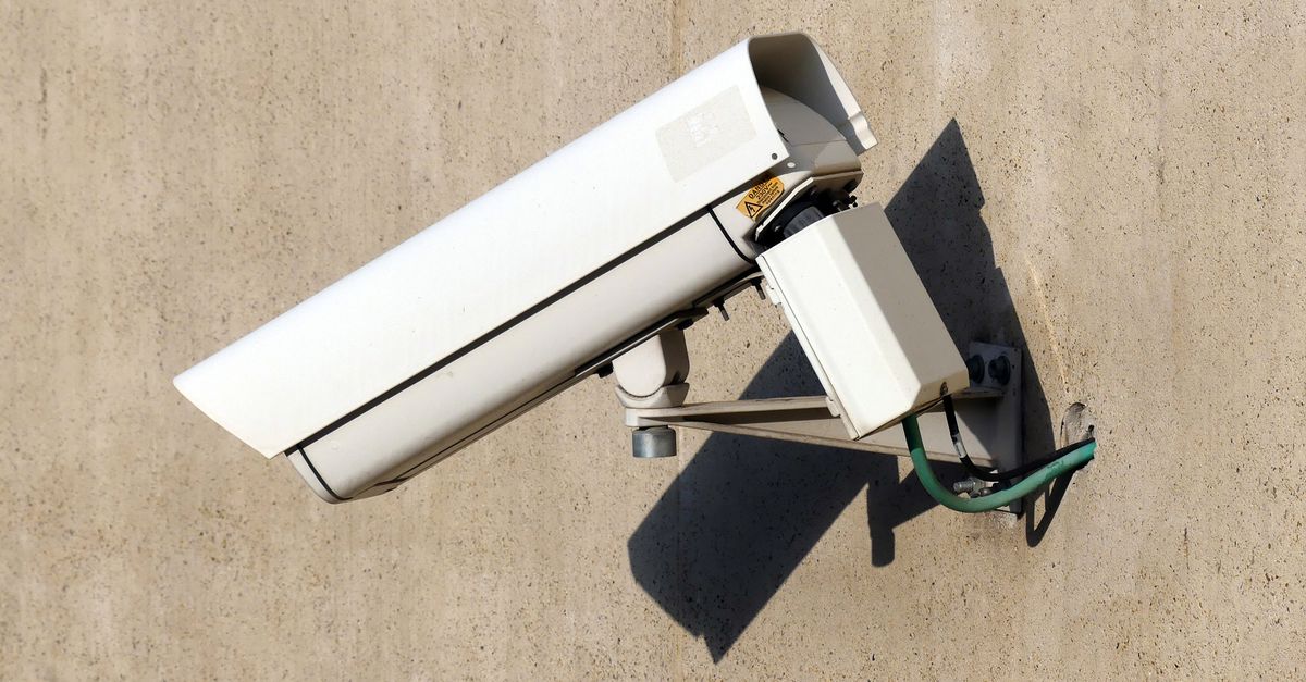 Close-up of a white security camera mounted on a beige wall in sunlight, emphasizing safety.