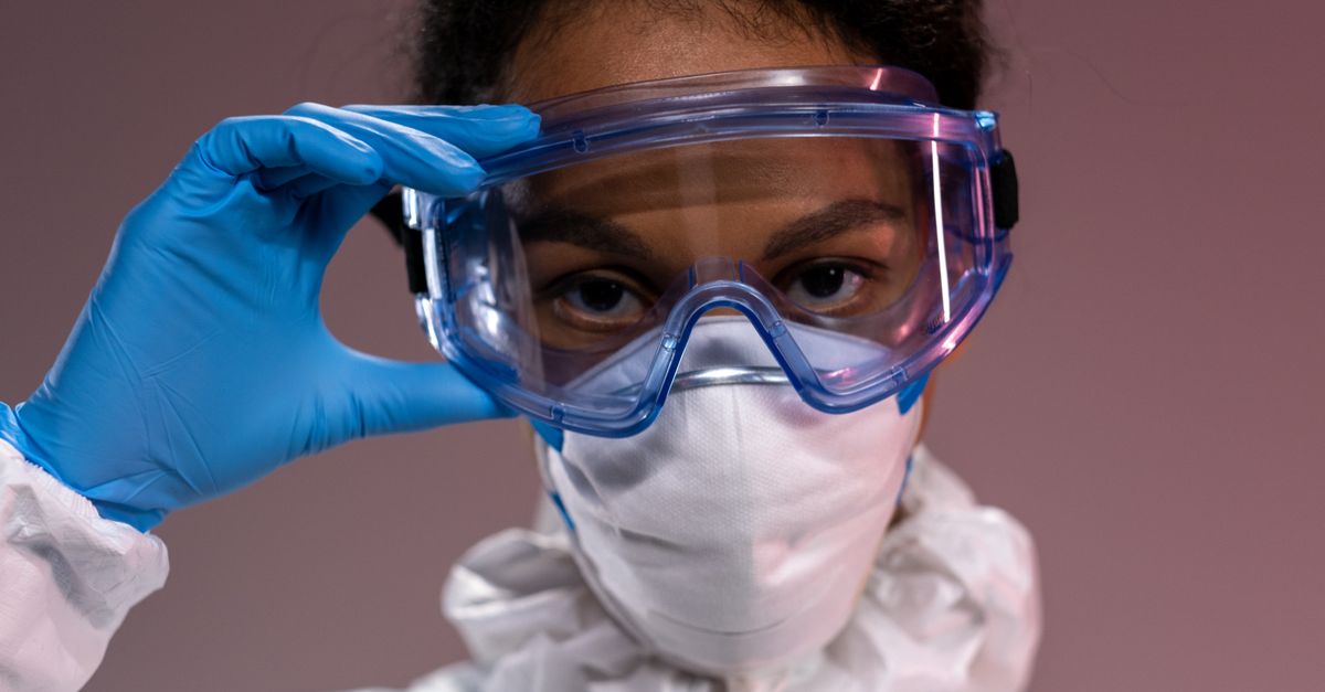 Close-up portrait of a healthcare worker wearing full protective equipment, eyeglasses, mask, and gloves.