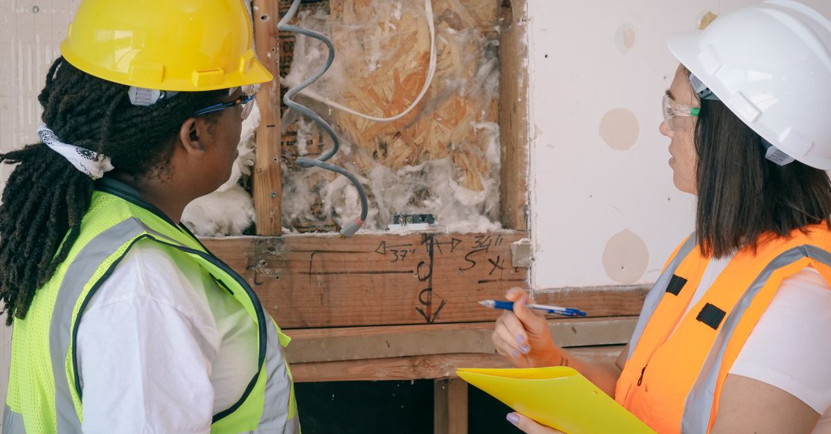 Two female engineers in safety gear reviewing construction plans onsite.