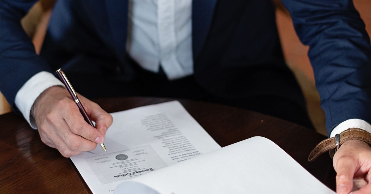 A professional individual signs legal documents at a desk in an office setting.