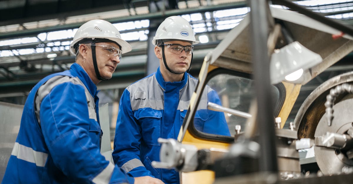 Two industrial workers in protective gear operate machinery in a factory setting.