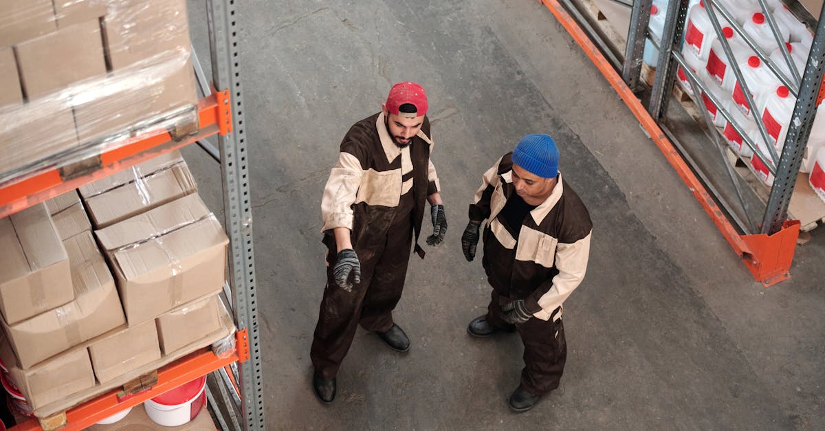 Two adult men in a warehouse communicating about storage logistics, surrounded by shelves of packages.