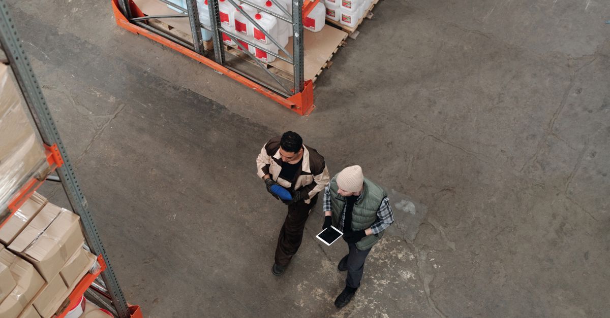 Two workers discussing inventory in a warehouse, using a digital tablet for coordination.