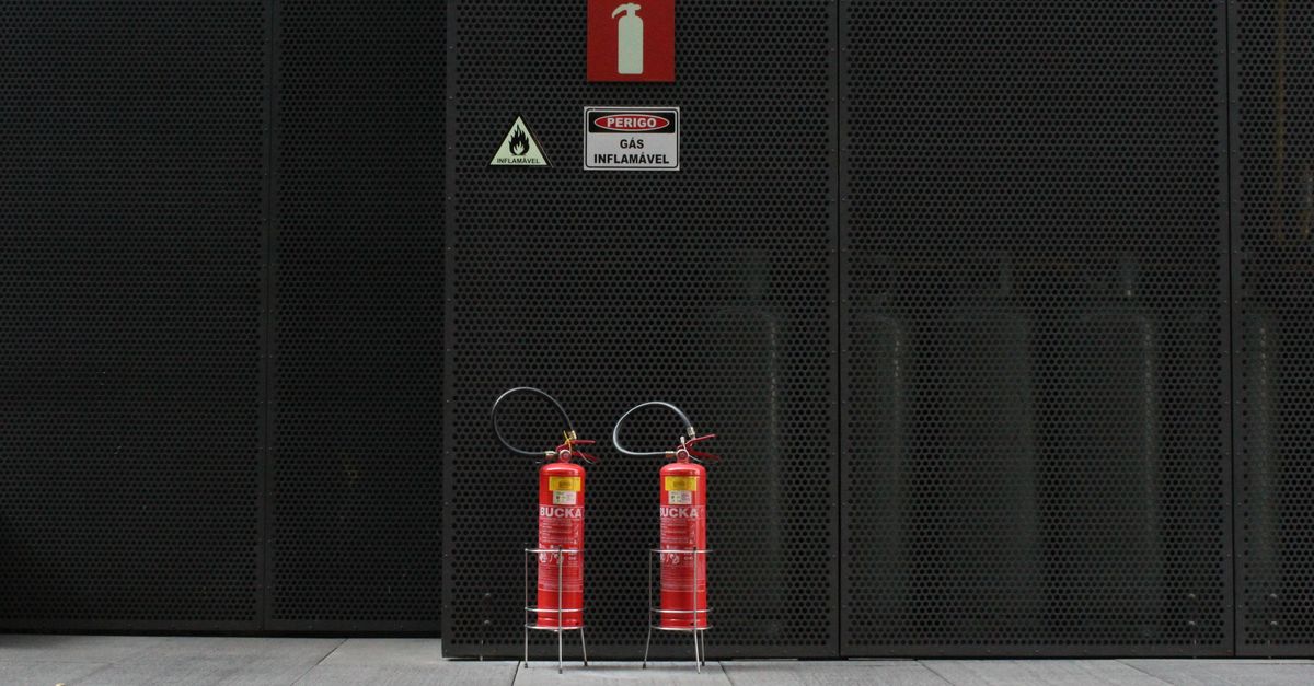 Red fire extinguishers against industrial metal wall with warning signs.
