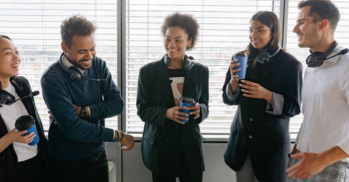 A diverse group of call center agents enjoying a casual break in the office, sharing laughs and hot drinks.