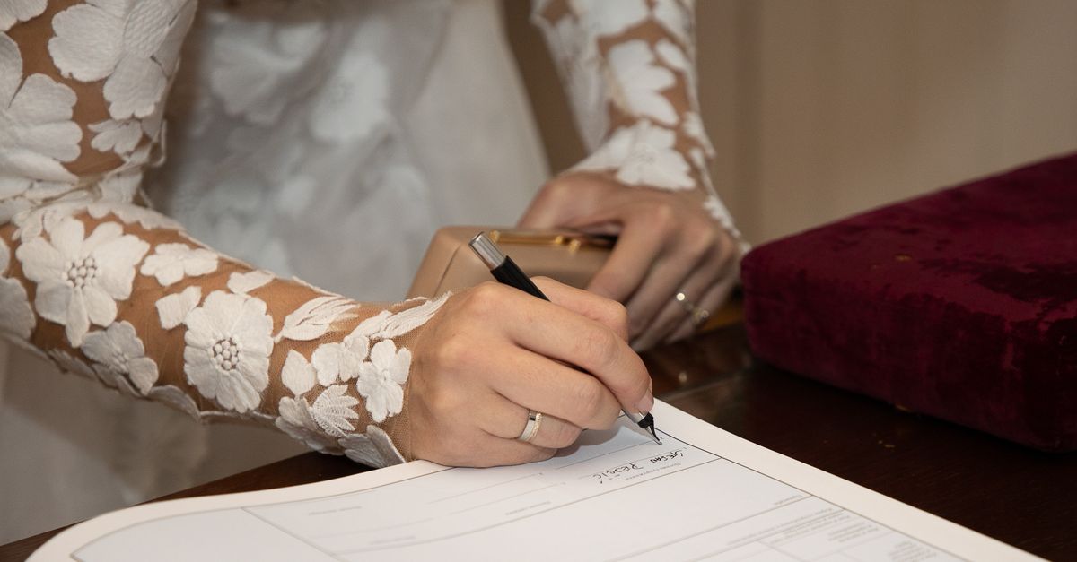 Bride in lace dress signing marriage certificate at wedding ceremony.