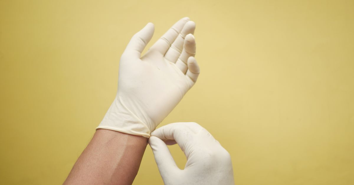 Close-up of hands putting on latex gloves against a yellow background.
