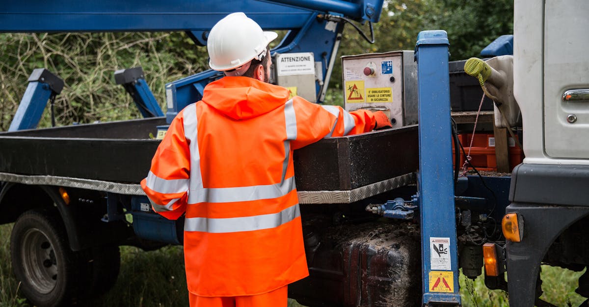 A worker in orange uniform and helmet controls machinery on site.