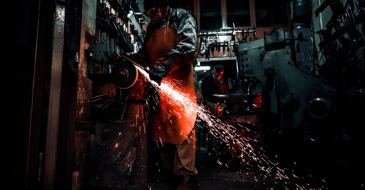 Metalworker using grinding machine in dimly lit workshop, sparks flying.