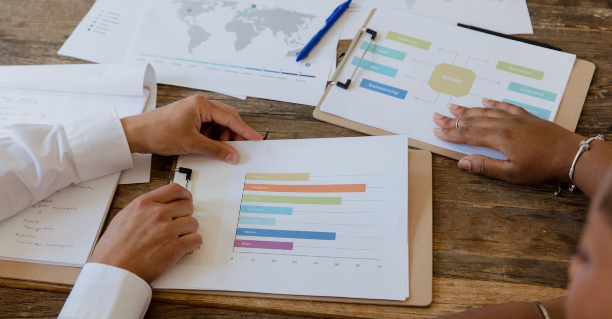 Top view of colleagues discussing charts and graphs on a wooden table during a business meeting.