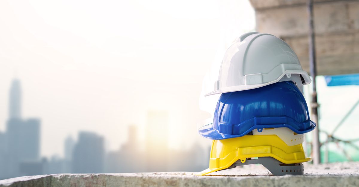 Three colorful safety helmets stacked on a concrete surface with city skyline in background.