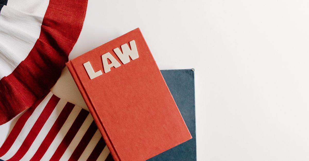 A flat lay of a red law book, American flag, and ribbon displaying patriotic themes.