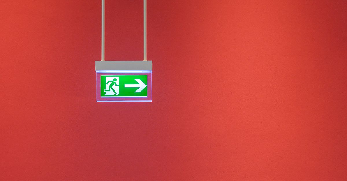 Green emergency exit sign with arrow on vibrant red wall, indicating direction for safety.