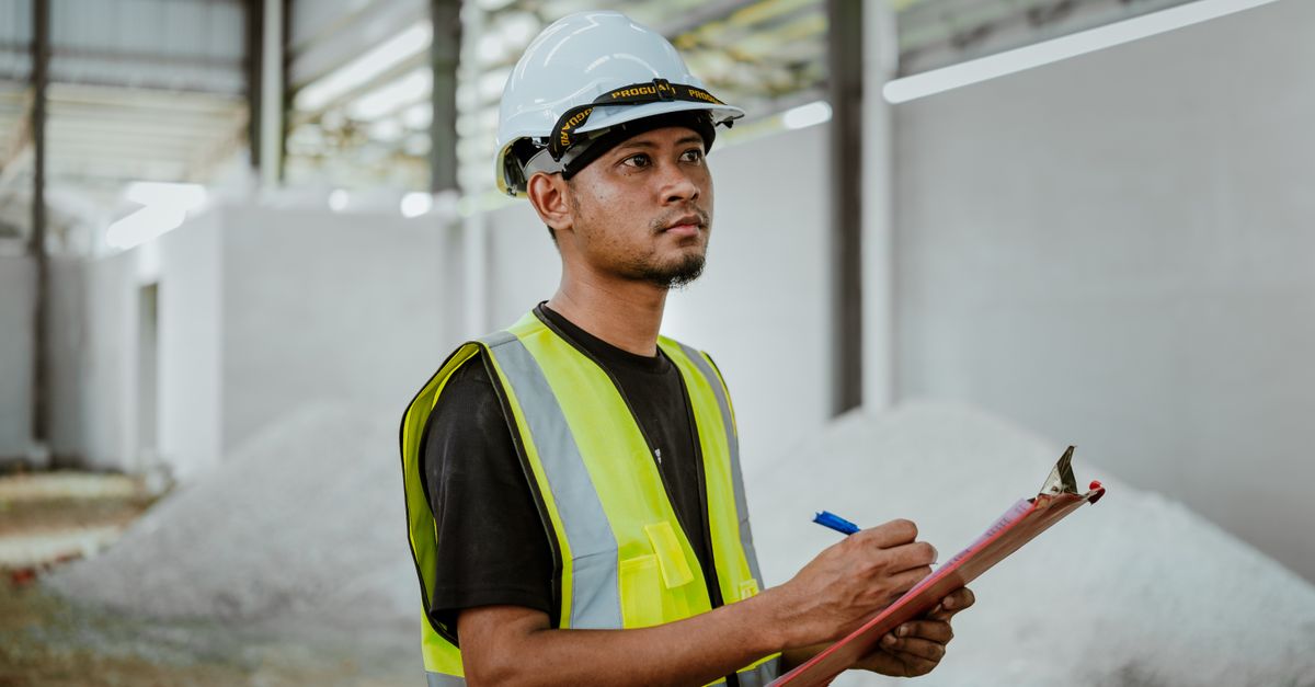 Asian construction worker in a factory setting, using a clipboard for inspection tasks in Banting, Malaysia.