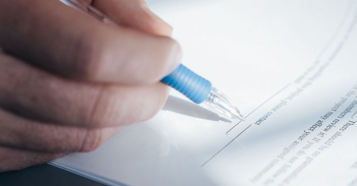 A close-up image showing a hand holding a pen while signing a document.