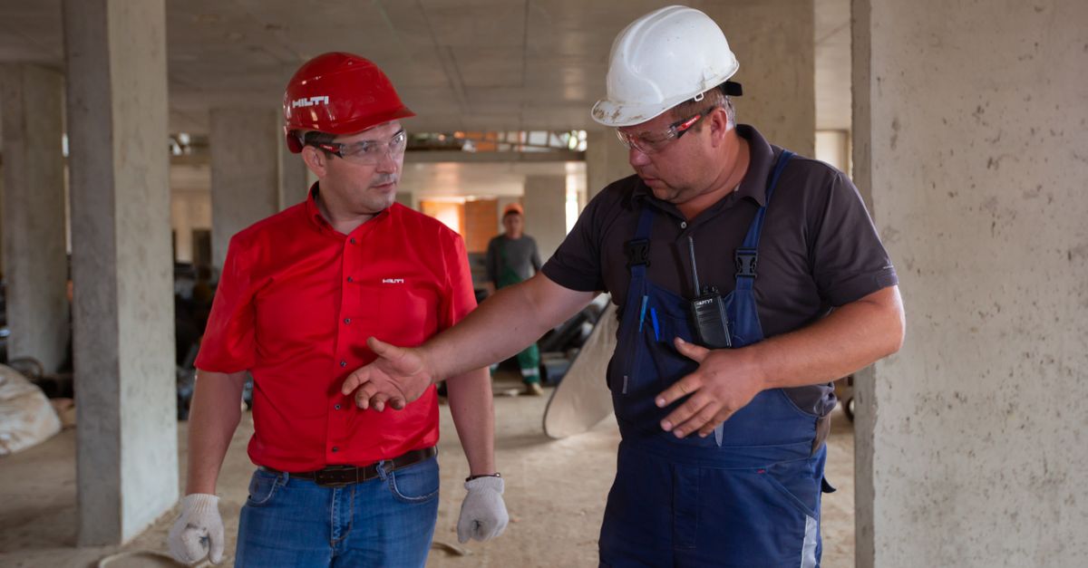 Two construction workers in safety gear discussing plans at a construction site.