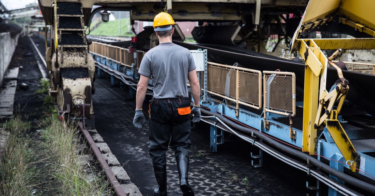 A worker in safety gear examines industrial machinery in an outdoor setting, showcasing industry work.