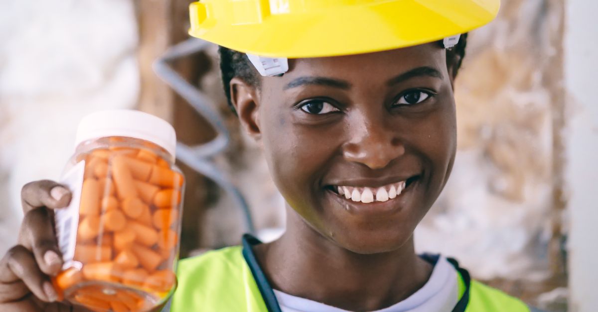 Smiling African American construction worker holding ear plugs and wearing PPE.