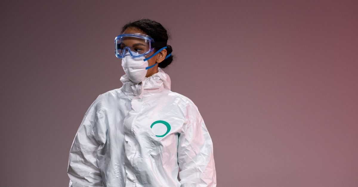 Medical professional in full protective suit with goggles and mask, studio setting.