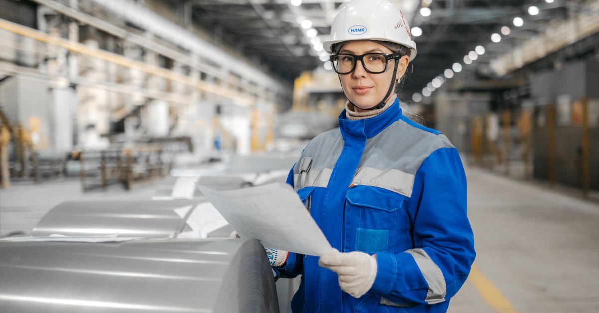 A female engineer wearing safety gear inspects machinery in an industrial factory setting.