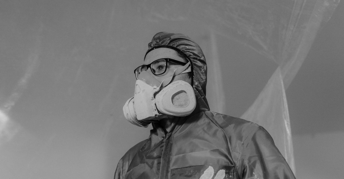 Worker wearing a gas mask and safety gear in a monochrome setting, emphasizing protection and safety.
