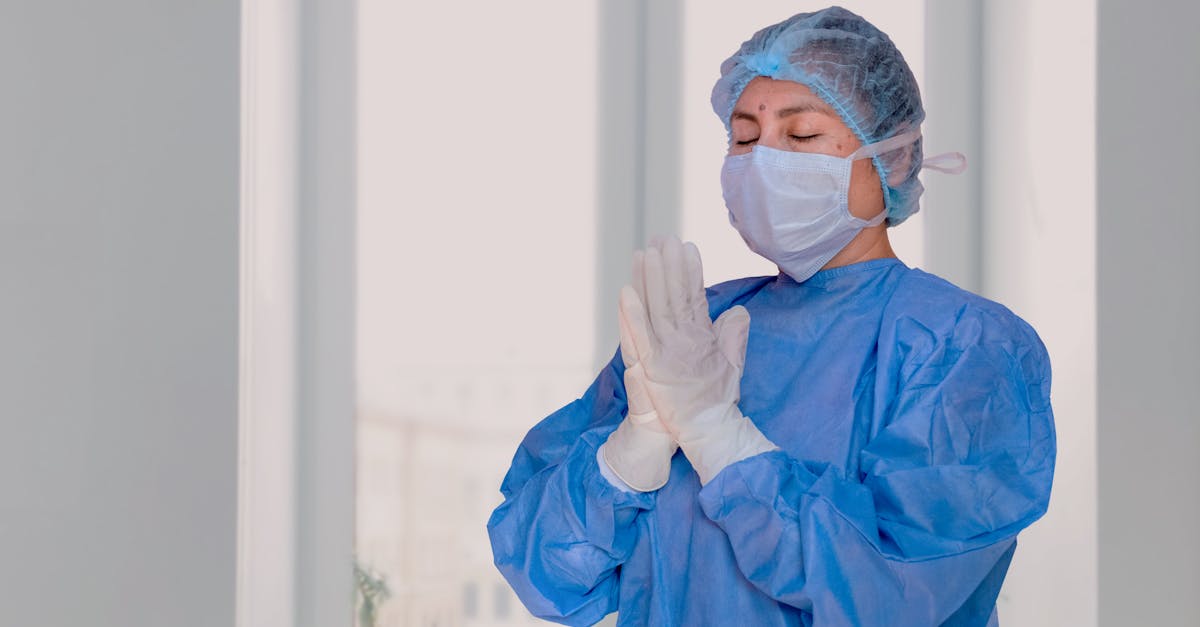 A healthcare worker in protective gear with praying hands, indoors.