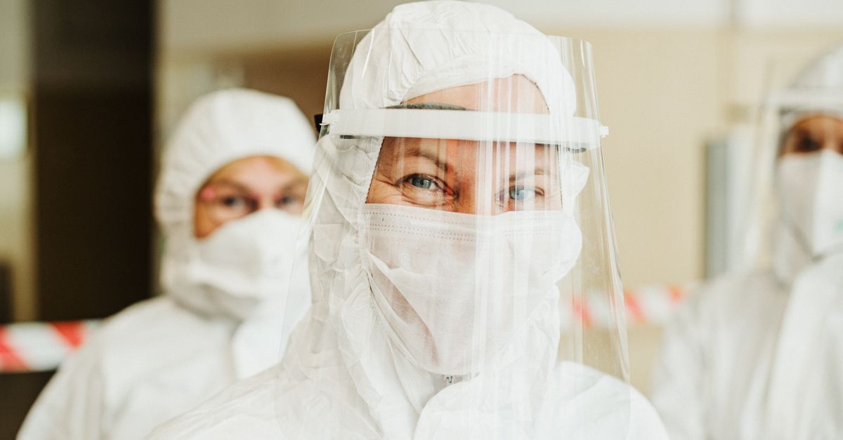 Healthcare workers wearing protective suits and face shields in hospital setting during pandemic.