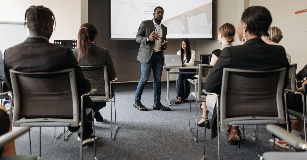 Diverse group attending a business seminar with a presenter and screen display.