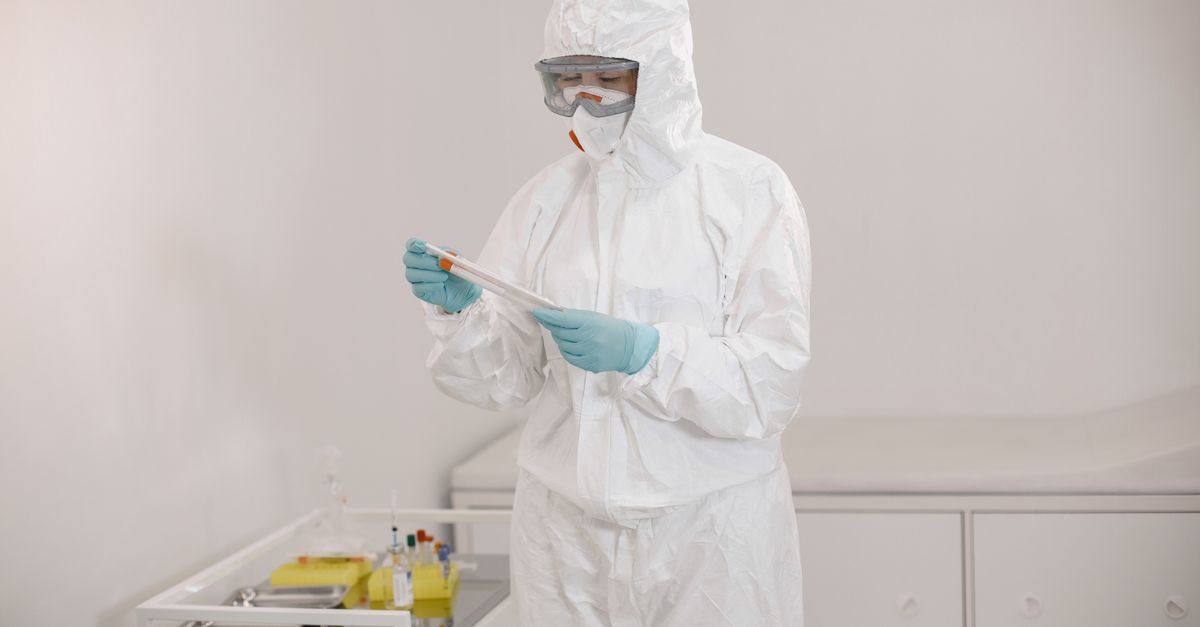 Scientist in a protective suit analyzing a test sample in a laboratory setting for safety and research purposes.