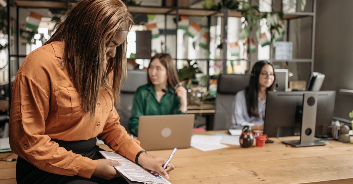 Three women collaborating in a modern office setting with laptops and documents.