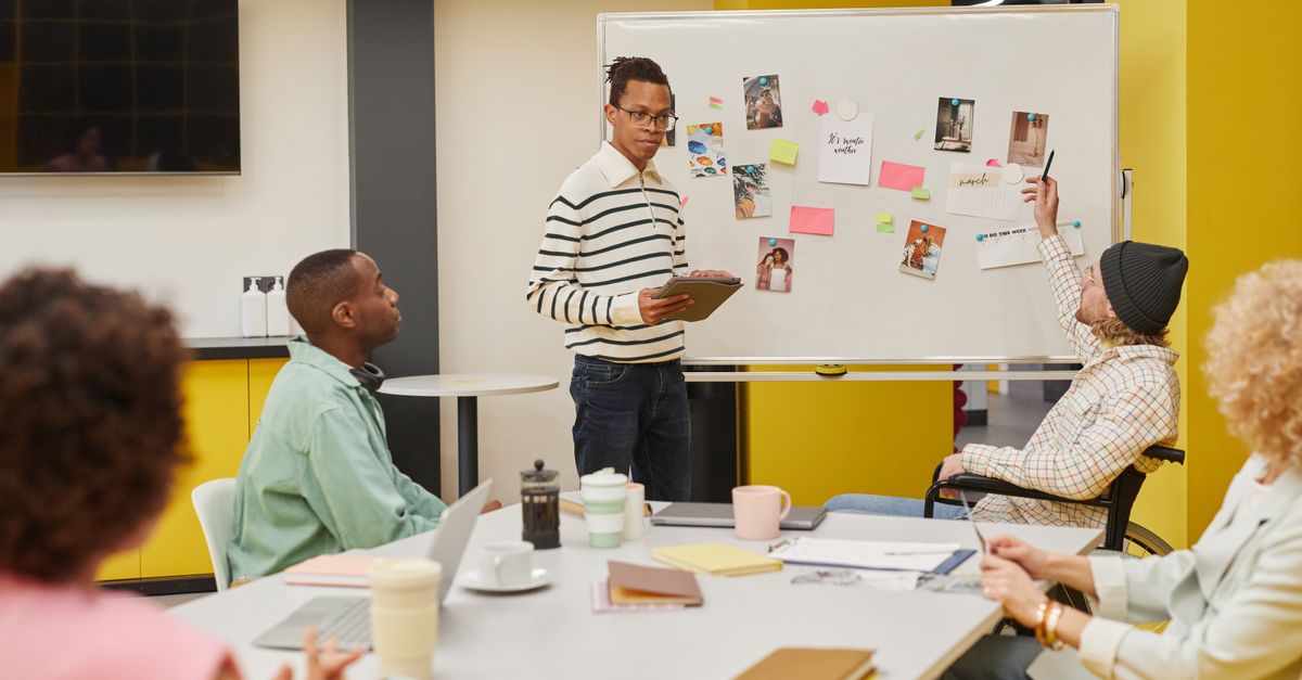 A diverse team engaged in a collaborative meeting around a whiteboard in a modern office setting.