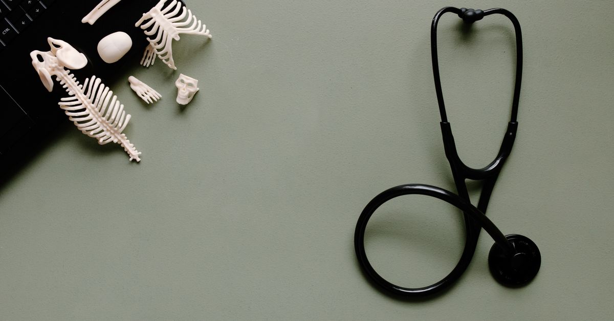 A flat lay of medical tools and small skeleton models on a green desk.