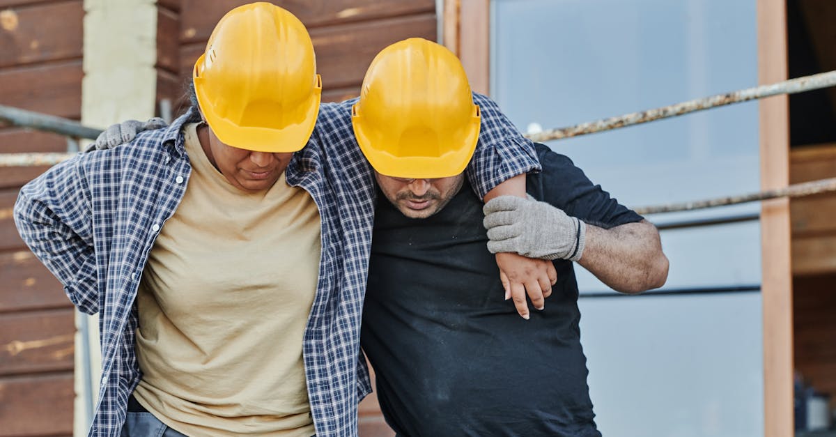 Two construction workers in hard hats assisting each other at a building site, highlighting teamwork.