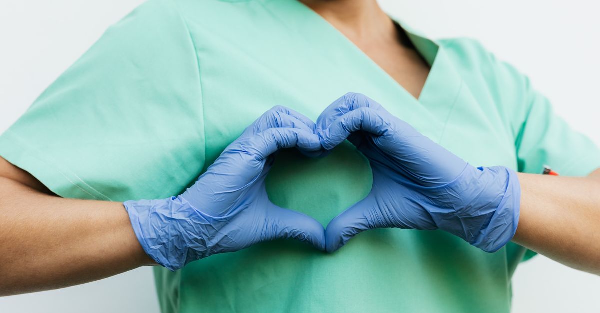 Nurse in blue gloves making a heart shape with hands, symbolizing compassion and care.