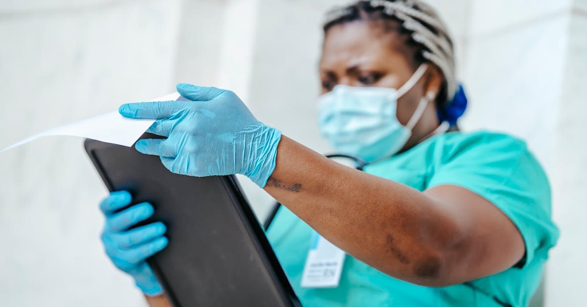Middle aged African American female doctor in disposable gloves and mask reading paper on clipboard